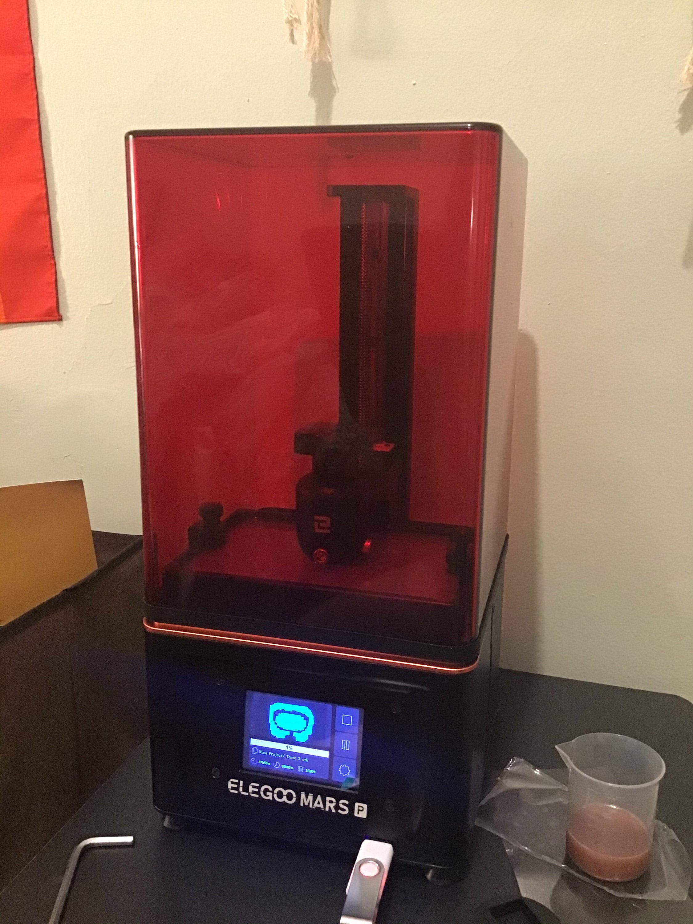 Image of an Elegoo Mars Pro, a 3D printer with a red tinted case and a blue LCD screen.