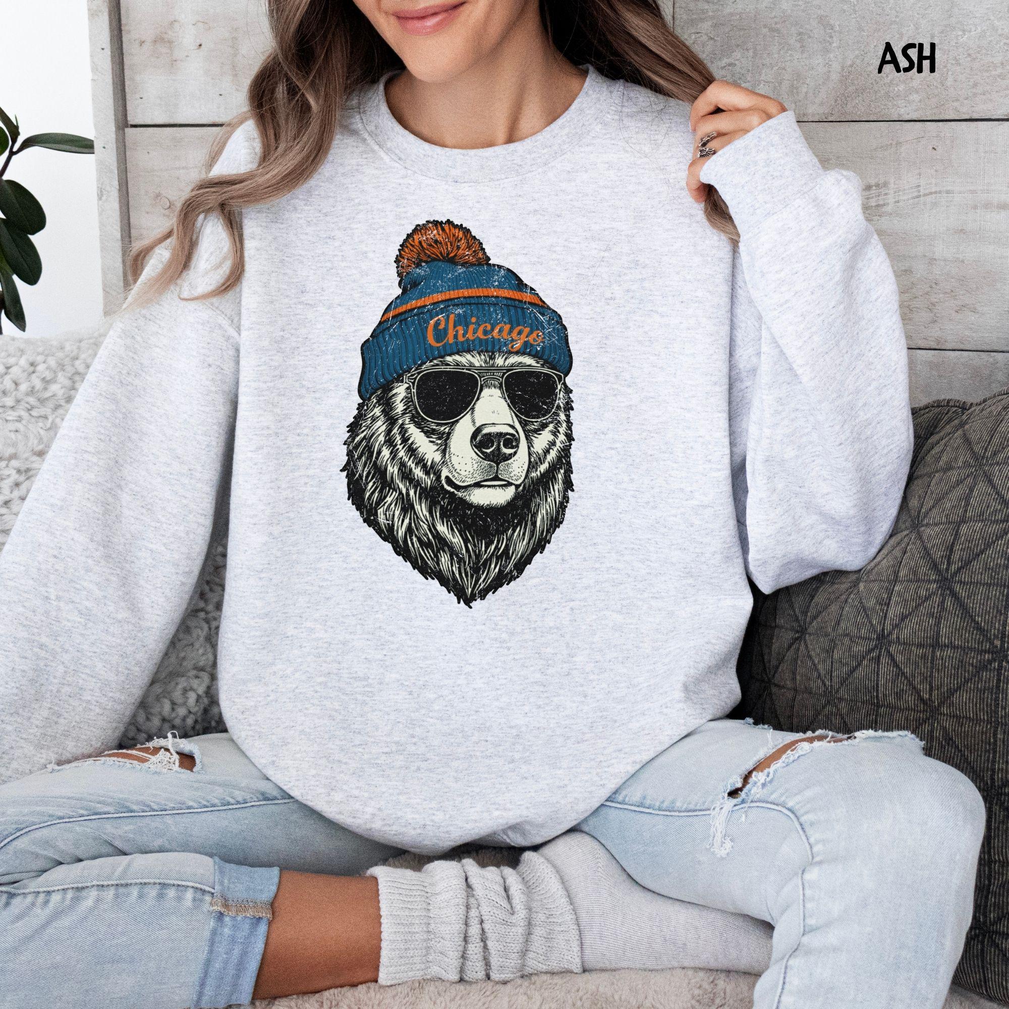 A detailed graphic of a black bear wearing a blue and orange Chicago beanie and black sunglasses, with a vintage, distressed texture