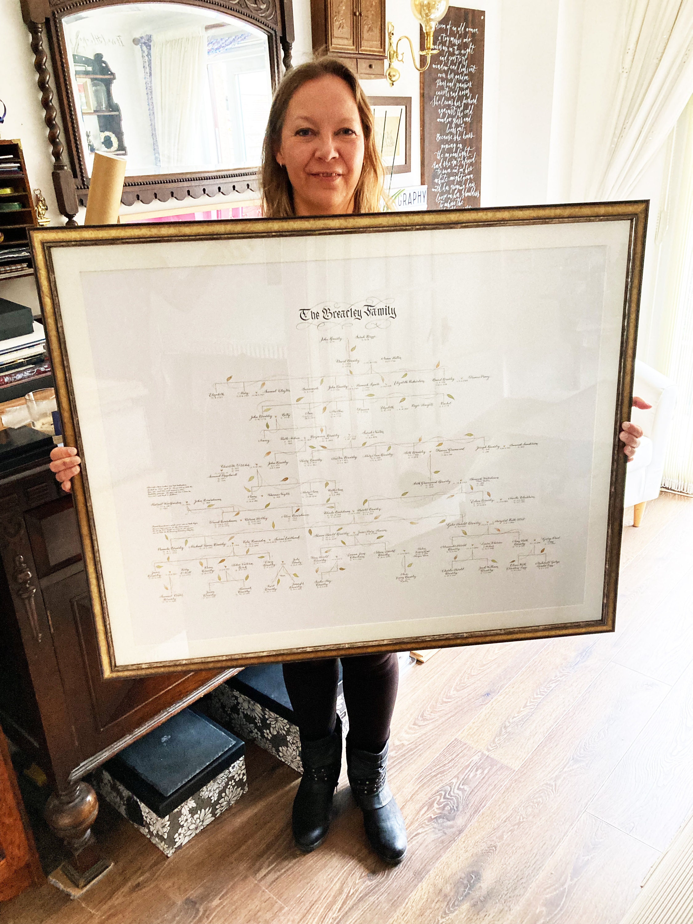 Handwritten family tree with 11 generations in a gold frame, held by the calligrapher