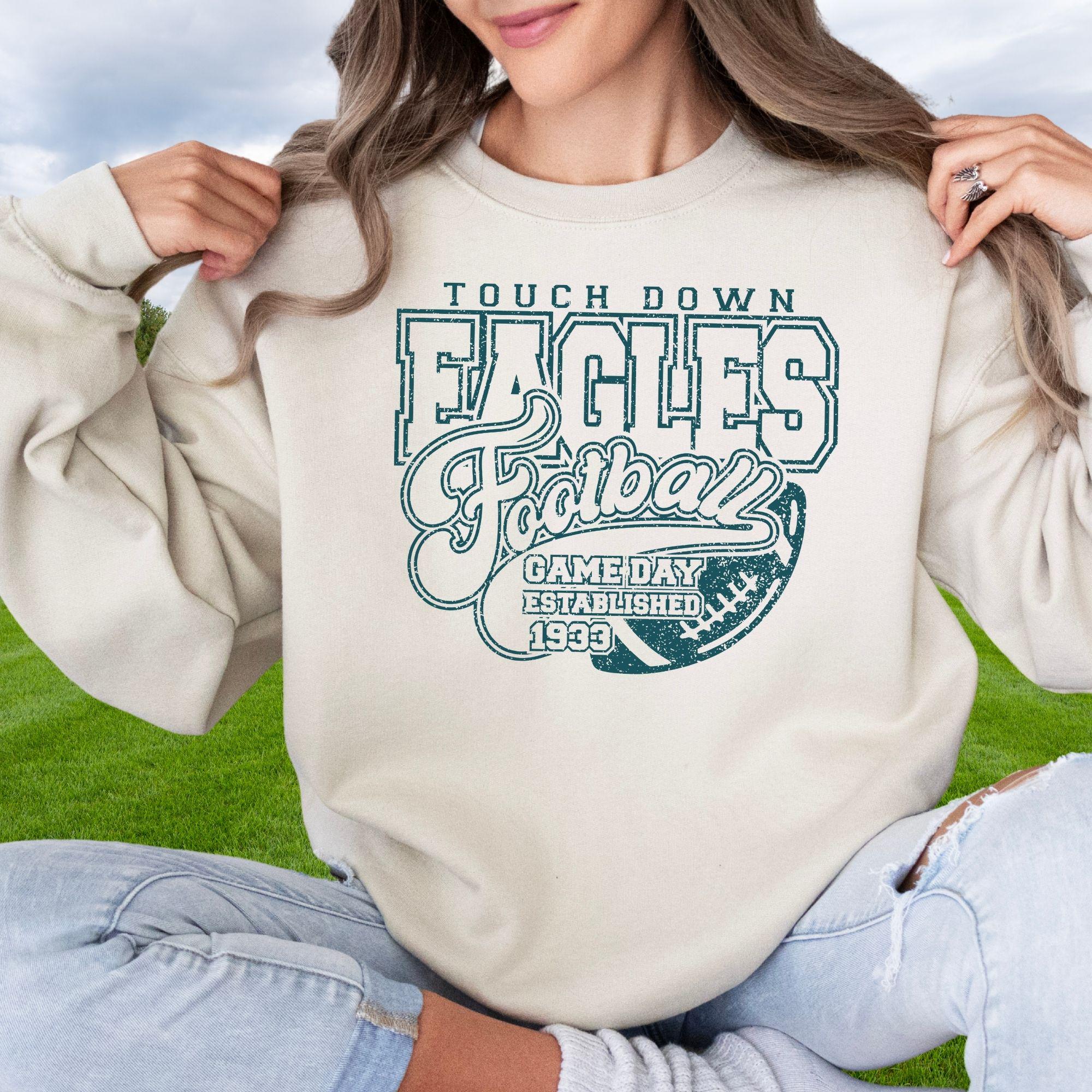 A close-up of the sand Touch Down Eagles graphic on a military green hoodie, showing the distressed texture of the design.