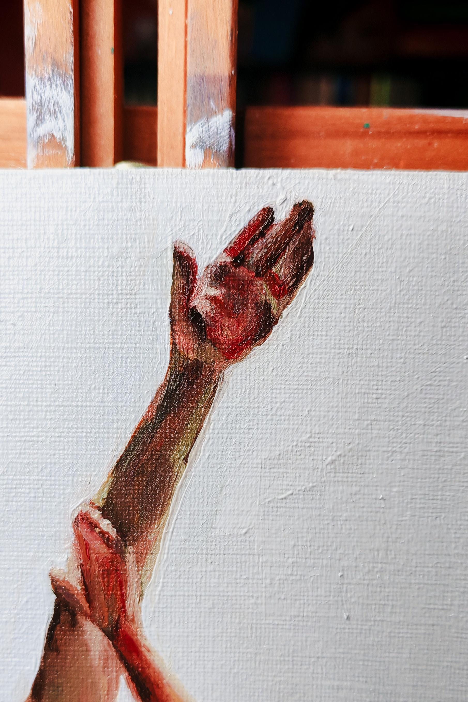 A close up of an oil painting on an easel showing an upstretched hand
