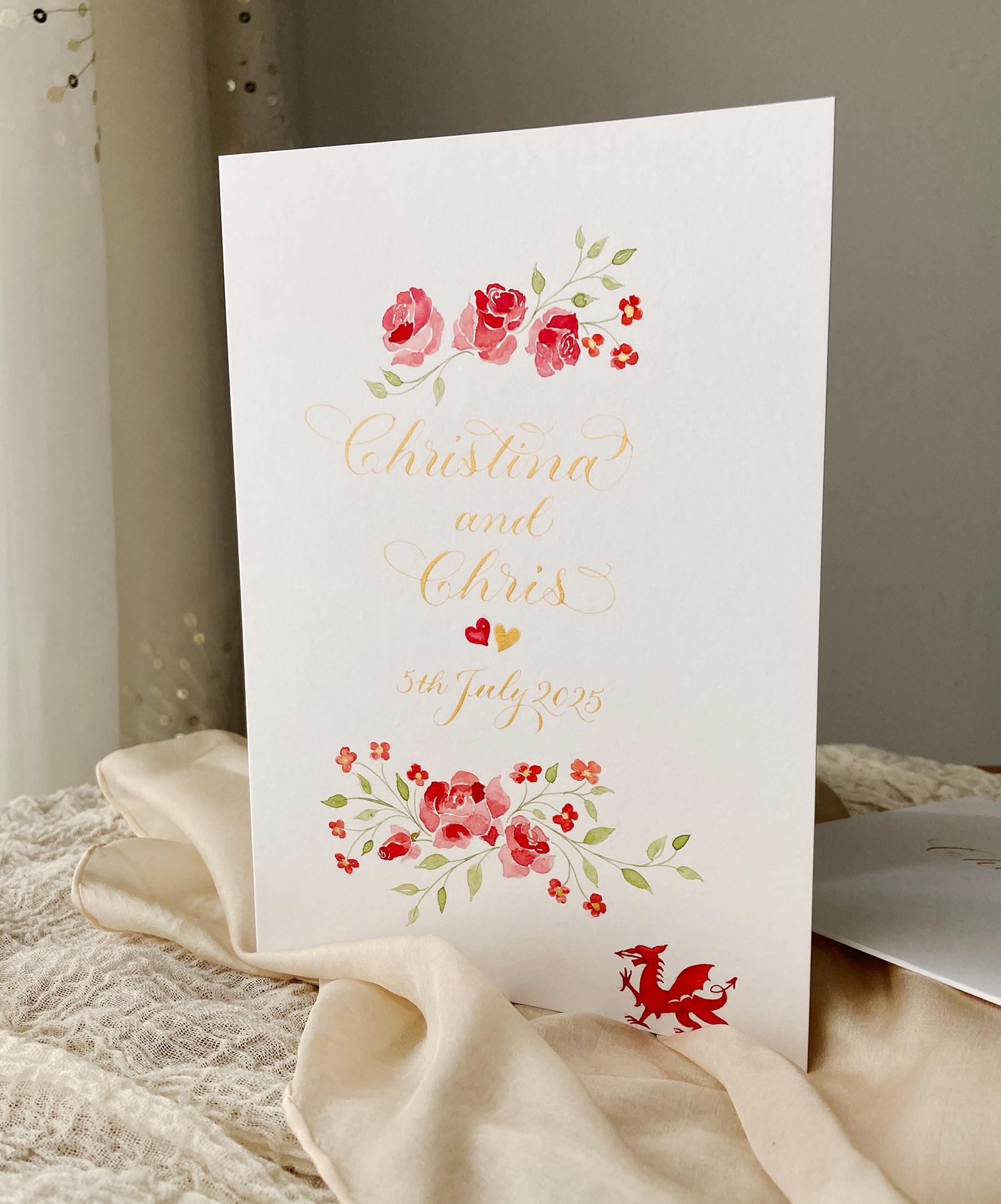 Bespoke calligraphy card with gold lettering, red roses and geums, and a little Welsh dragon
