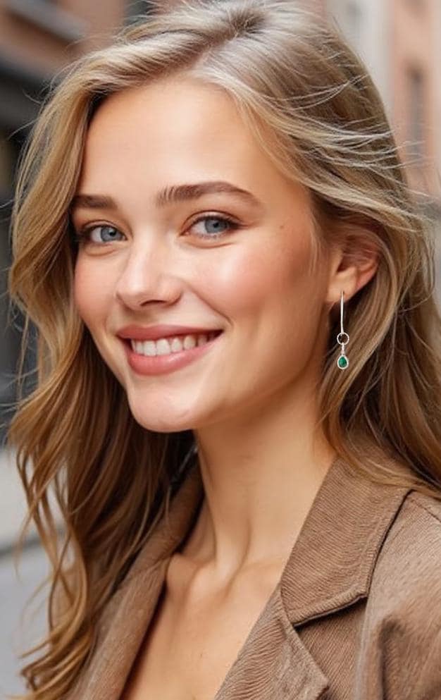 Woman wearing emerald dangle earrings, long silver earrings styled with beige business suit.
