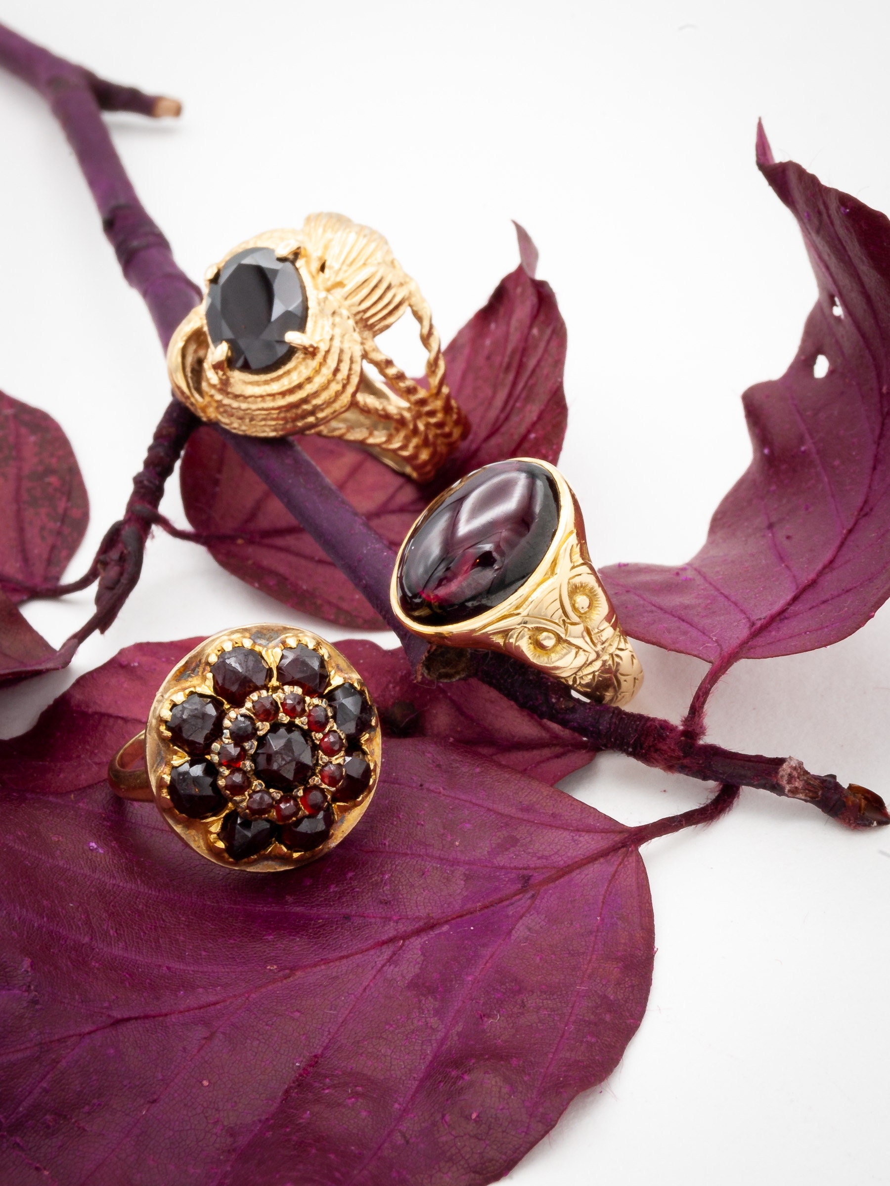 Three Garnet and Gold Vintage Rings with Cabochon and Faceted gemstones on Wine Red Leaves