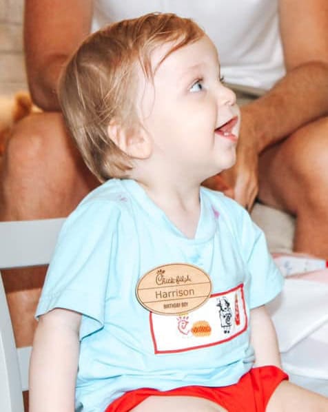 A toddler with a wondrously curious expression, wearing a maple hardwood chick-fil-a name tag and a Chick-fil-A t-shirt