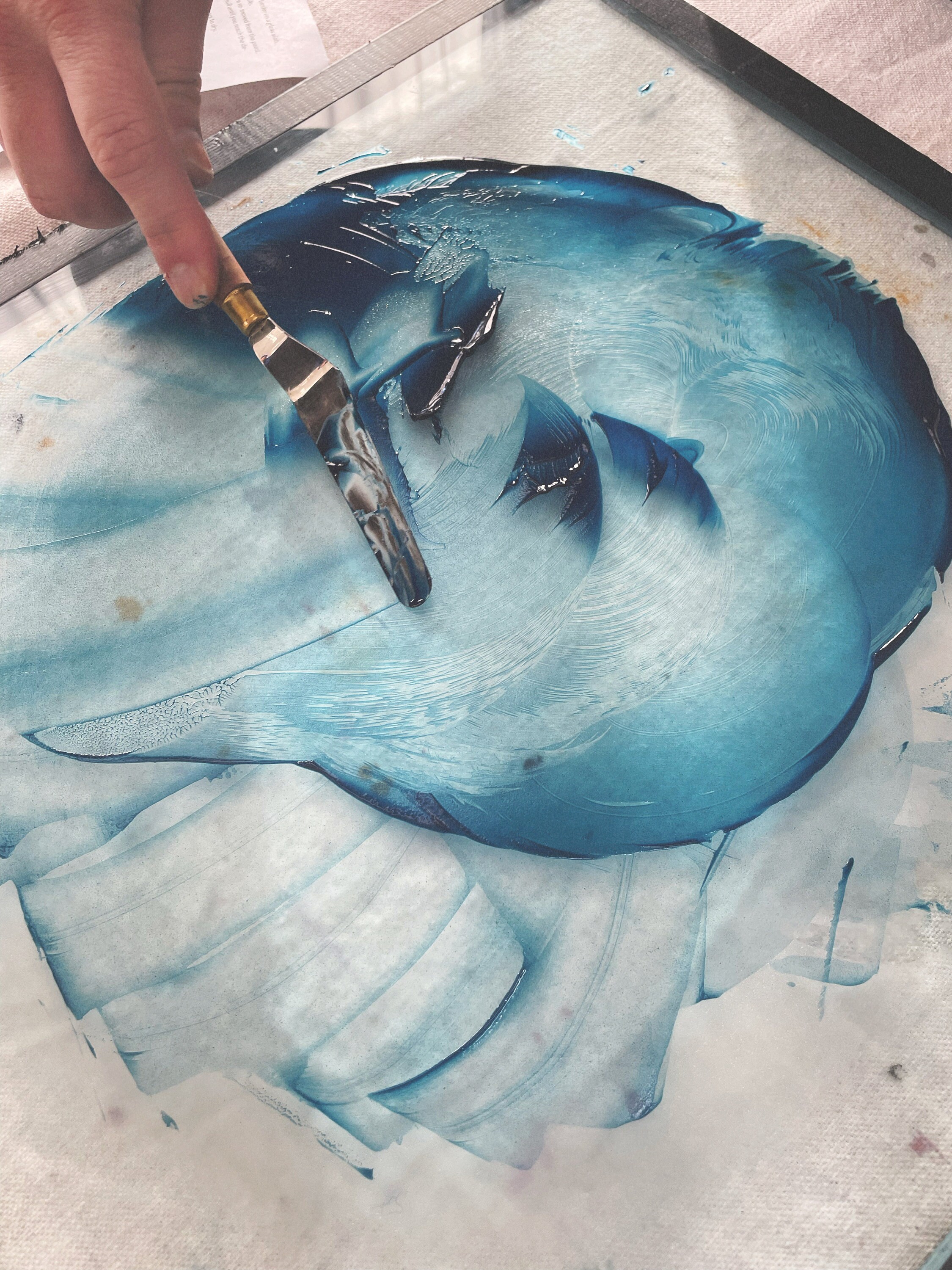 Using a palette knife on the glass slab to scrape together the watercolor weve made.