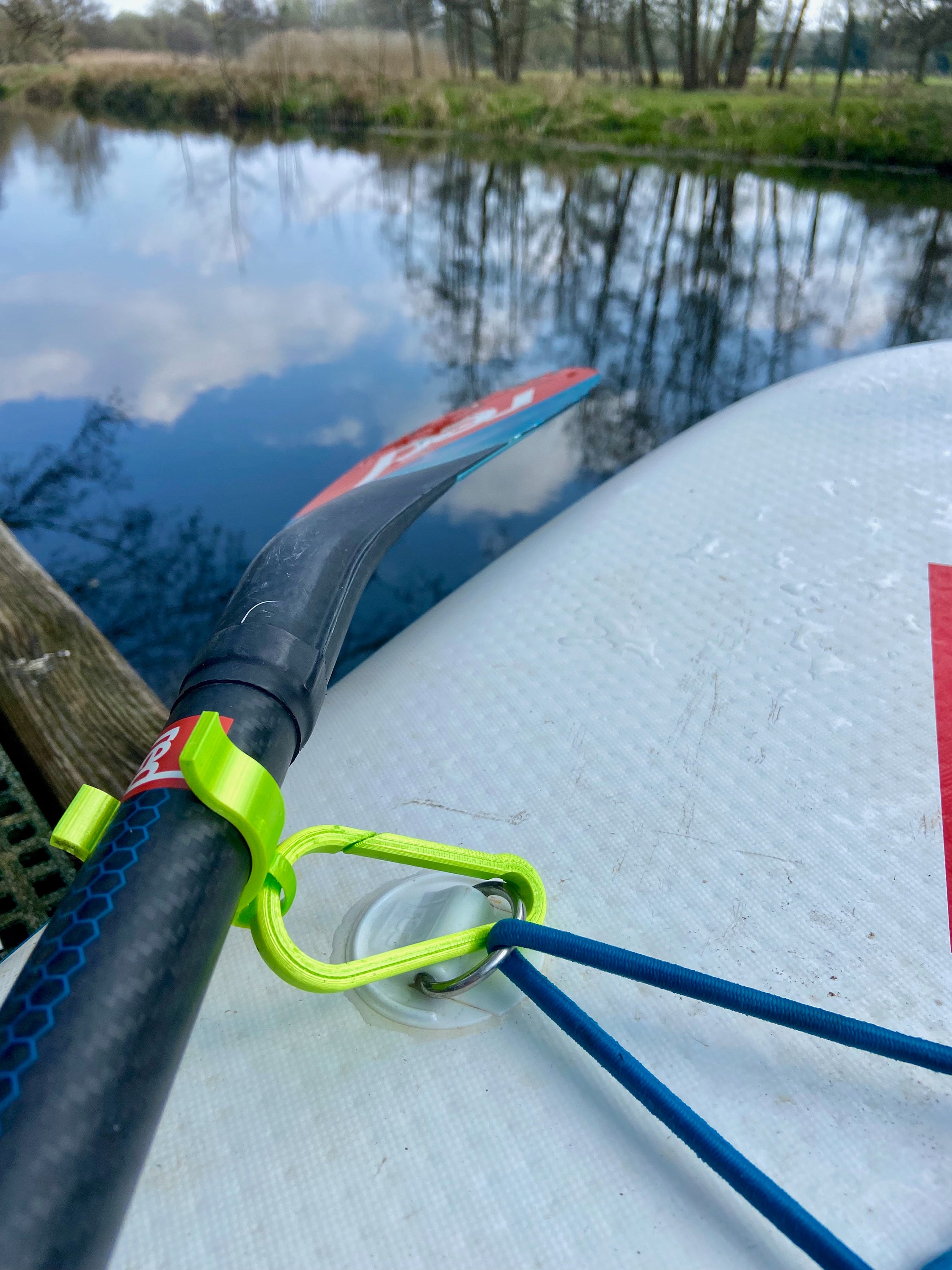 A paddle board on the side of a river with the paddle clipped onto the board