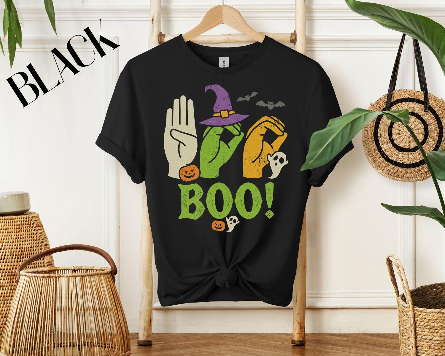 A vintage-style graphic design spelling out the word BOO. The B and Os are formed by hands using American Sign Language, decorated with a witch hat, pumpkins, and ghosts for a Halloween theme.