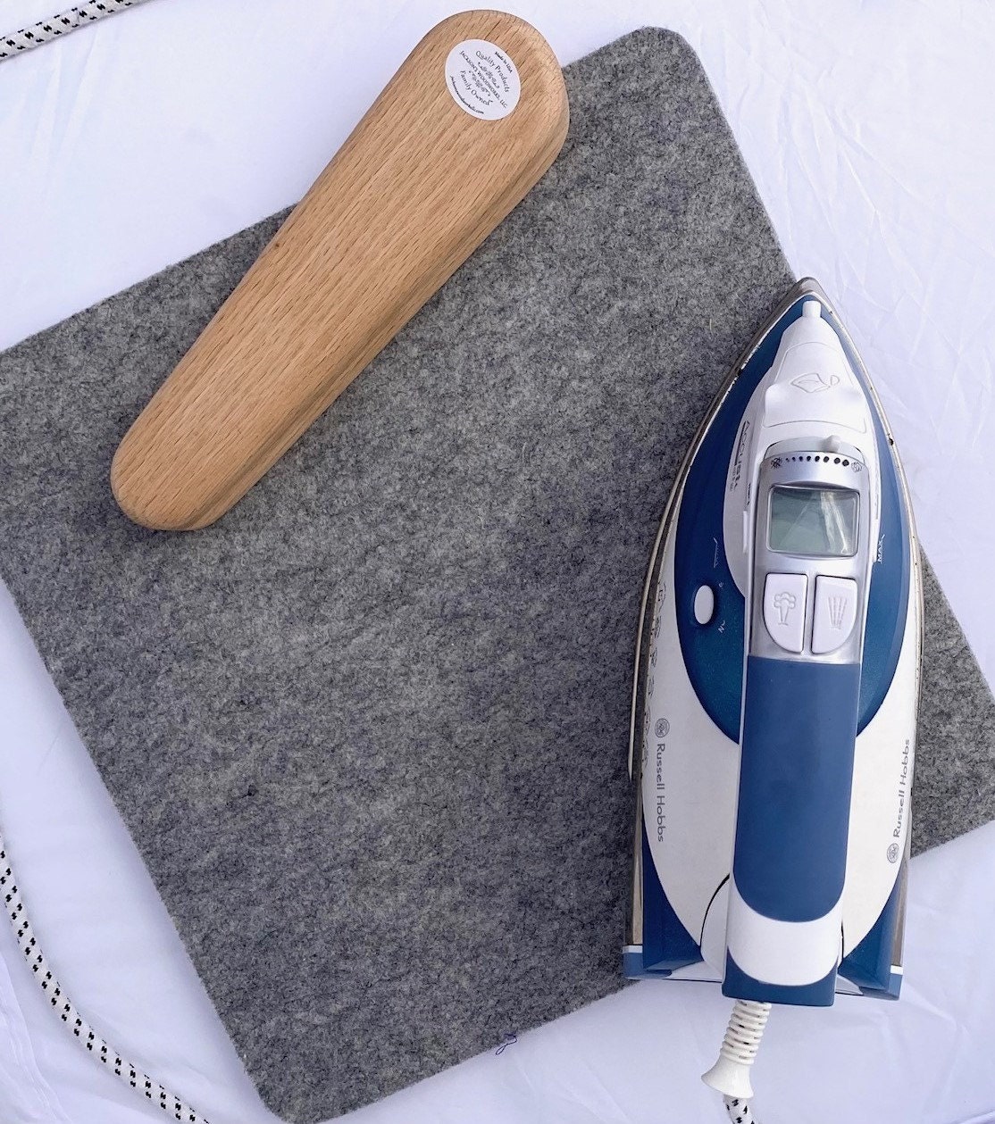 An iron and a tailors clapper sitting on a wool pressing mat.