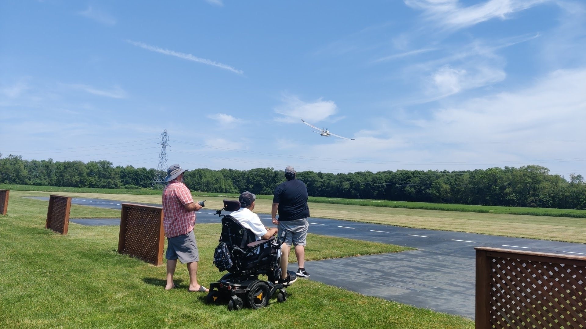 Two able bodied and one wheelchair user having fun flying an RC plane on an RC flying field