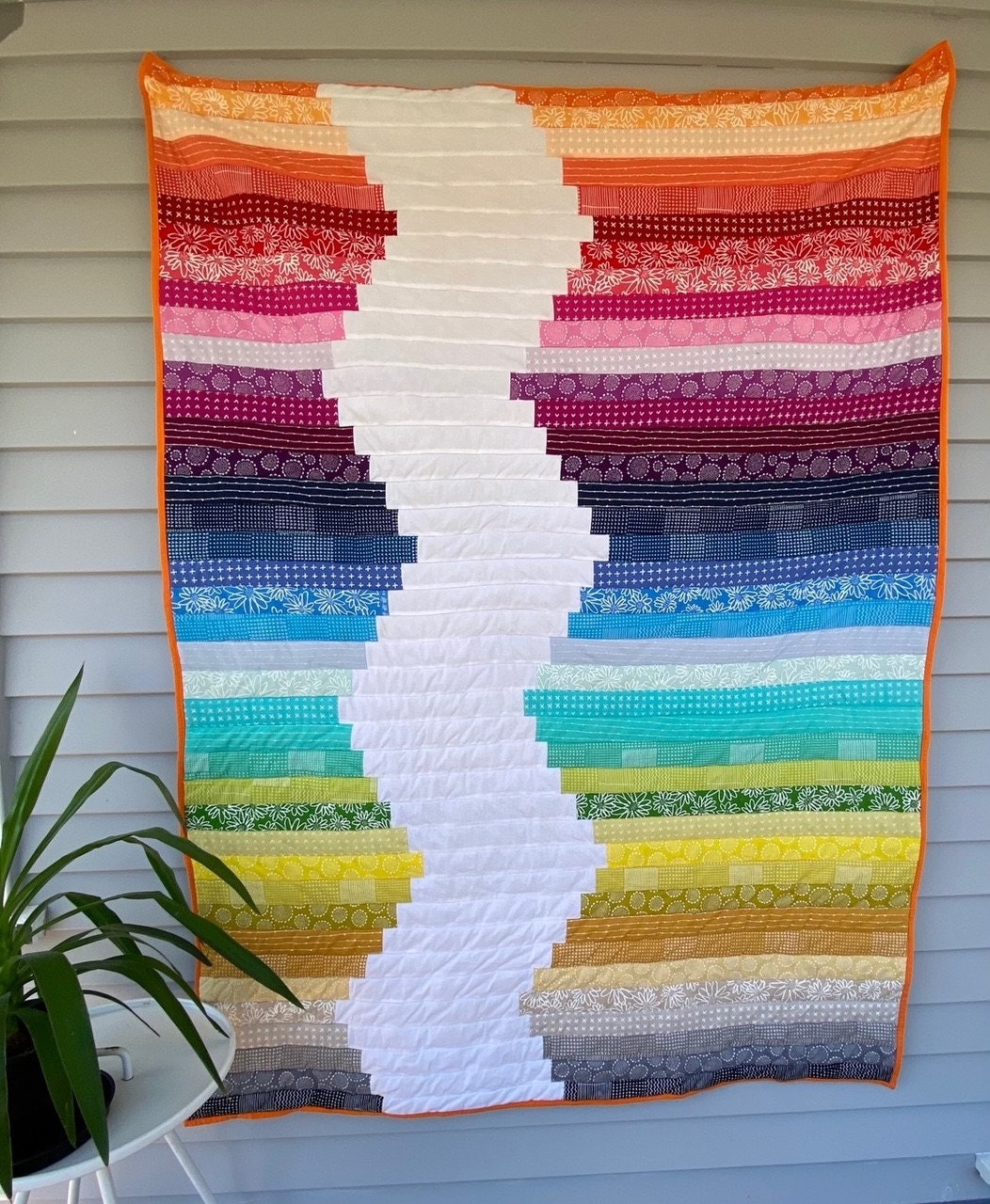 This is a very popular jelly roll quilt displayed on a wall. It has an array of beautiful coloured fabrics and a zig zag of white through the middle of the quilt. Quilt Along starts on July 1st 2020.