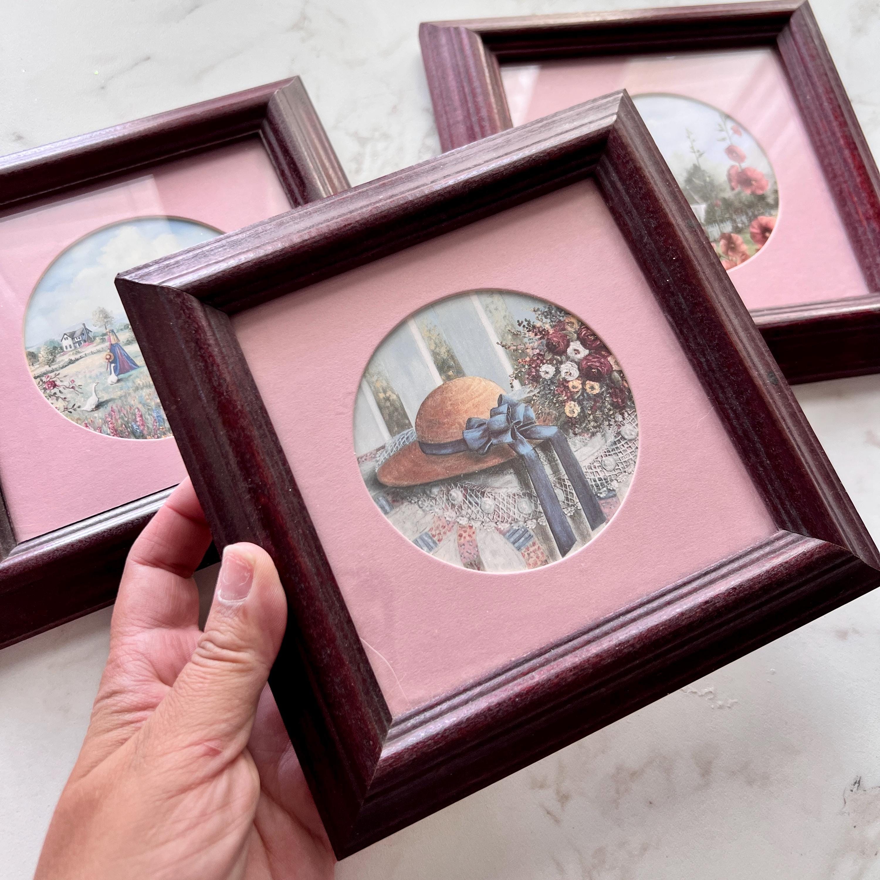 Set of three small vintage square frames with pink mats and circular art prints, featuring a countryside hat, flowers, and garden scenes.