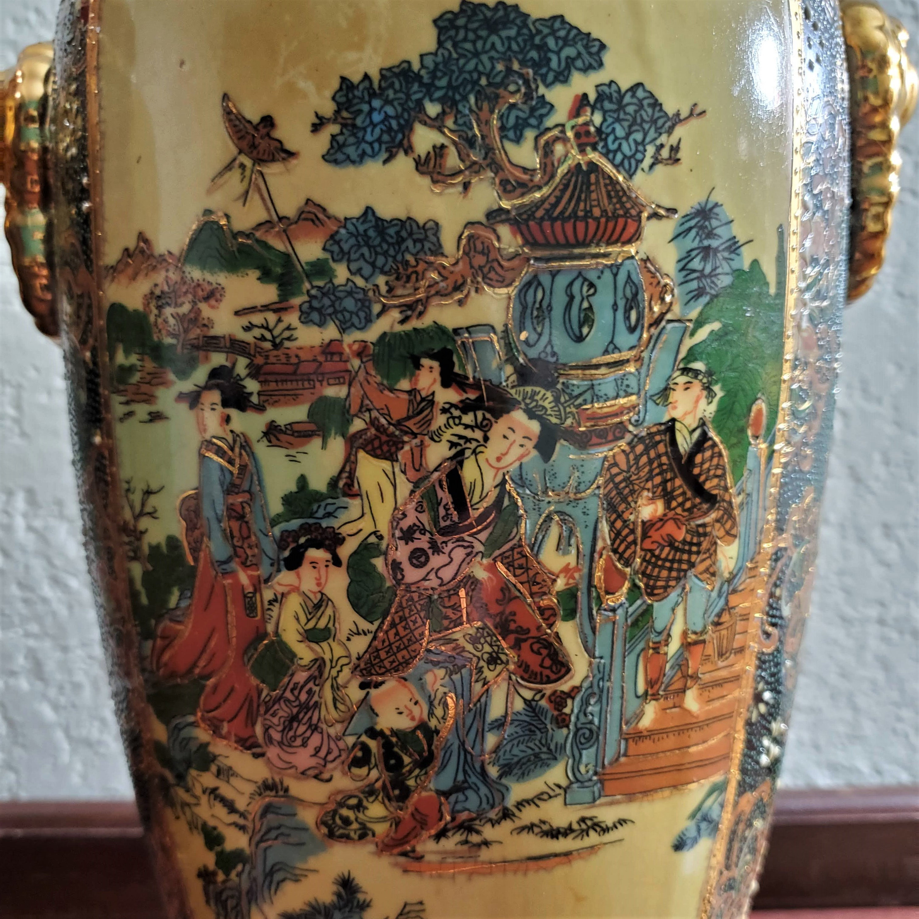 This lamp features a beautifully painted scene of a geisha and her companions in a garden, with intricate details and soft blue, brown, orange, and pink hues. The raised gold trim adds a touch of elegance, while the sturdy wooden base ensures stability. Perfect for adding a touch of Japanese artistry to any room.