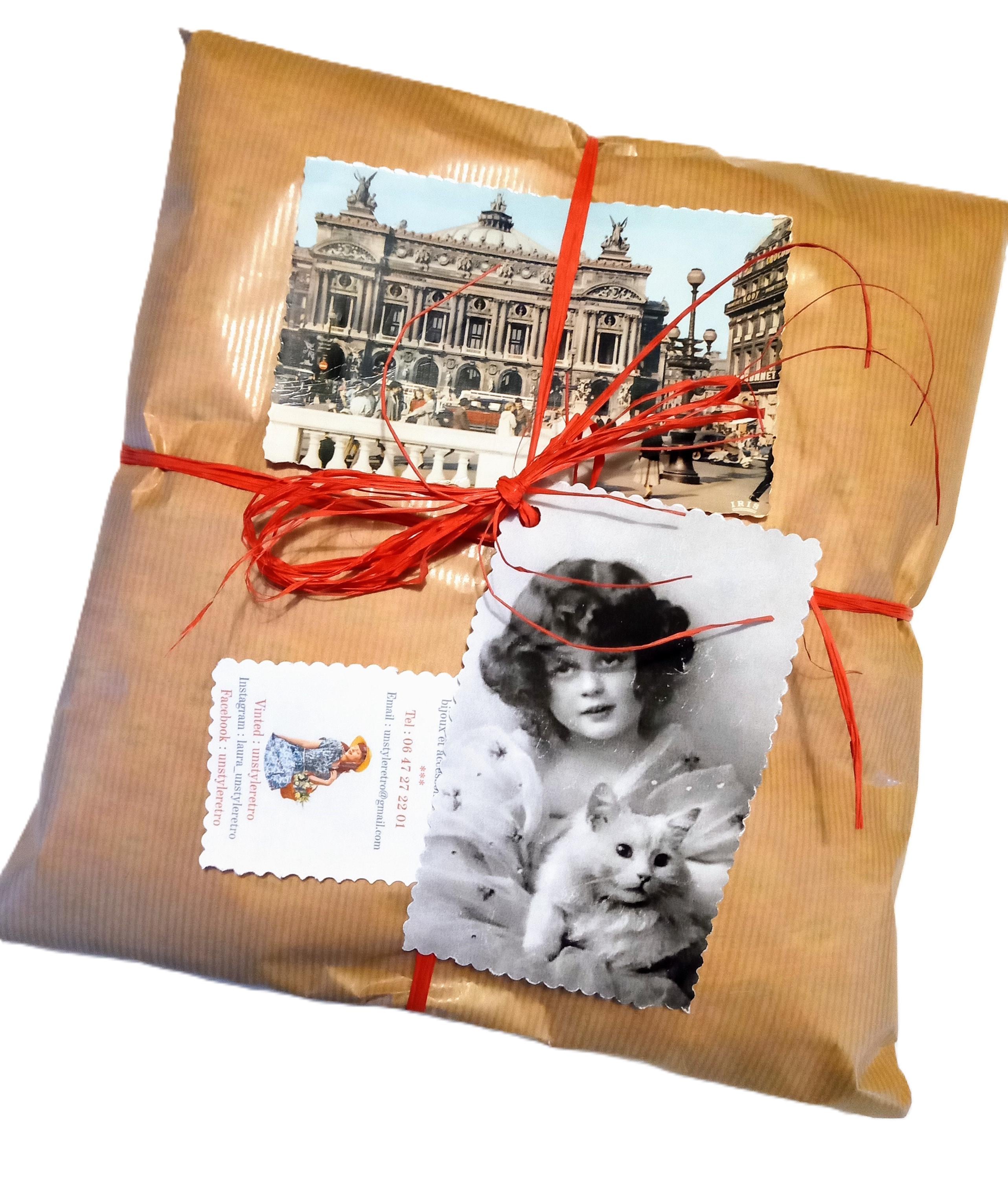 Packaging vintage éco-responsable de la boutique Un Style Rétro : colis emballé dans du papier kraft marron de la marque claire fontaine fabriqué en France, entouré dune ficelle en raphia rouge naturel. Le paquet est décoré dune carte postale ancienne de lOpéra de Paris et dune photo dart noir et blanc vintage dune jeune femme avec un chat blanc. Carte de visite artisanale de Laura Siméand.