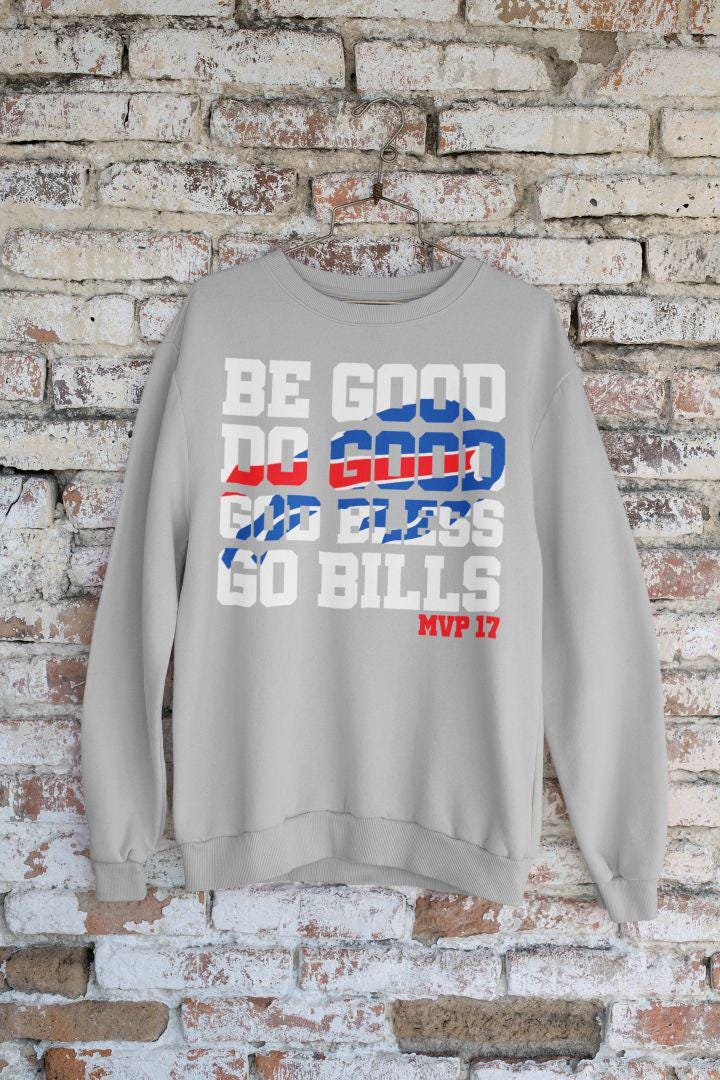 A cozy gray sweatshirt with a Be Good Do Good Buffalo football design hanging against a brick wall.