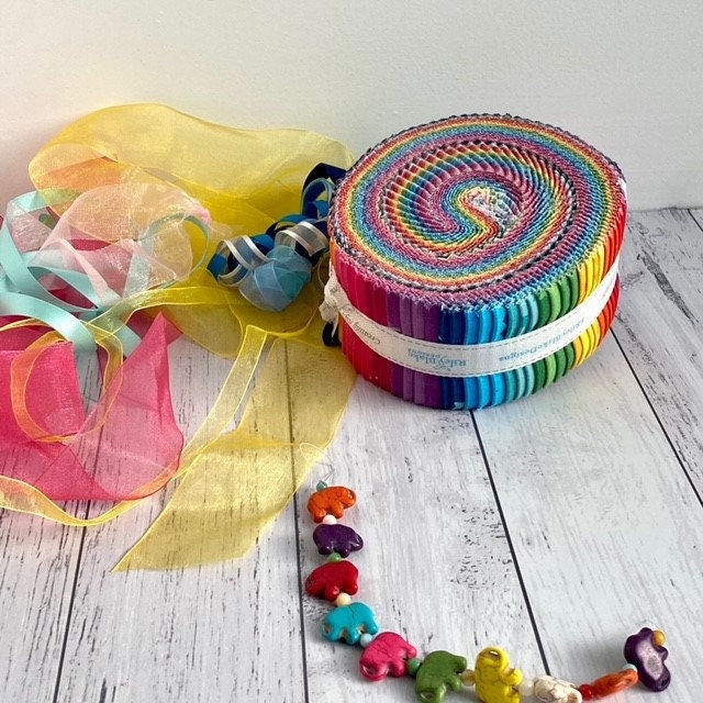A Rolie Polie of Create Fabric by Quiet Play ready for use in the River Rapids Quilt Along - a quilt along for beginner quilters, as well as more experienced quilters. The Jelly roll is surrounded by a small elephant bracelet and soft soft chiffon ribbons.