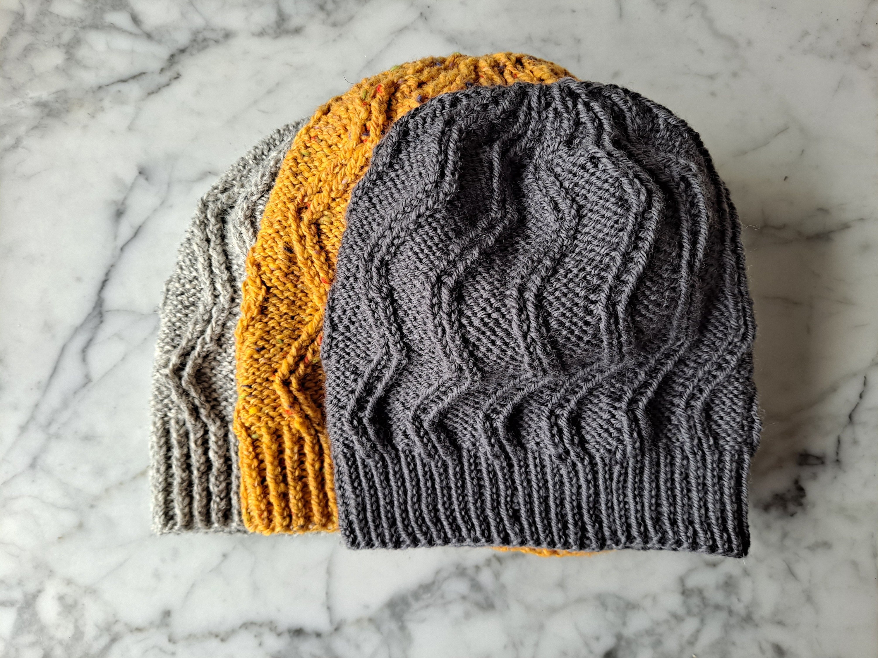 Three Beirt Beanie hats lie flat on a marble background.