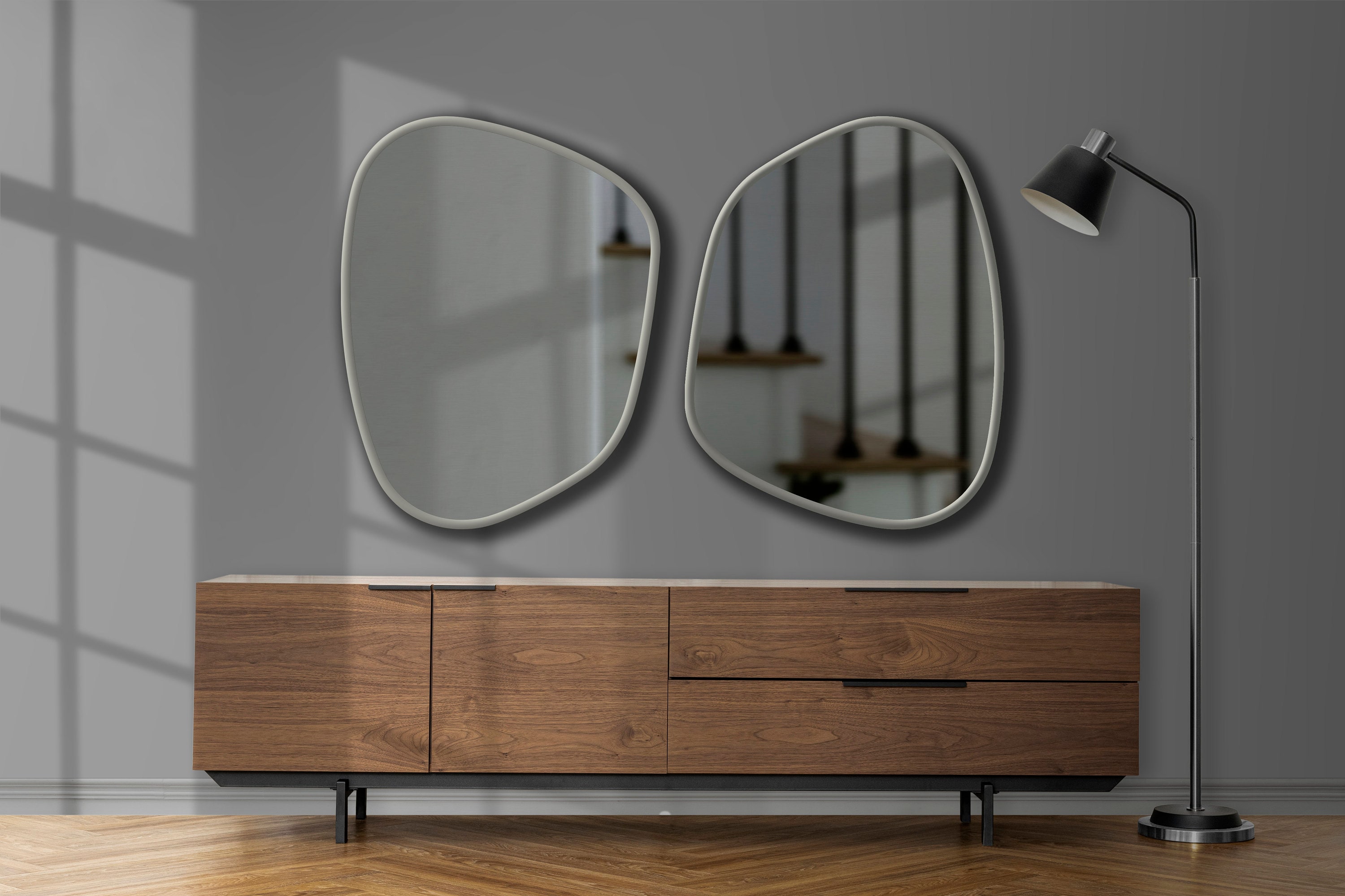 Two asymmetrical mirrors with silver frame hung on the wall of a living room above a wood drawer.