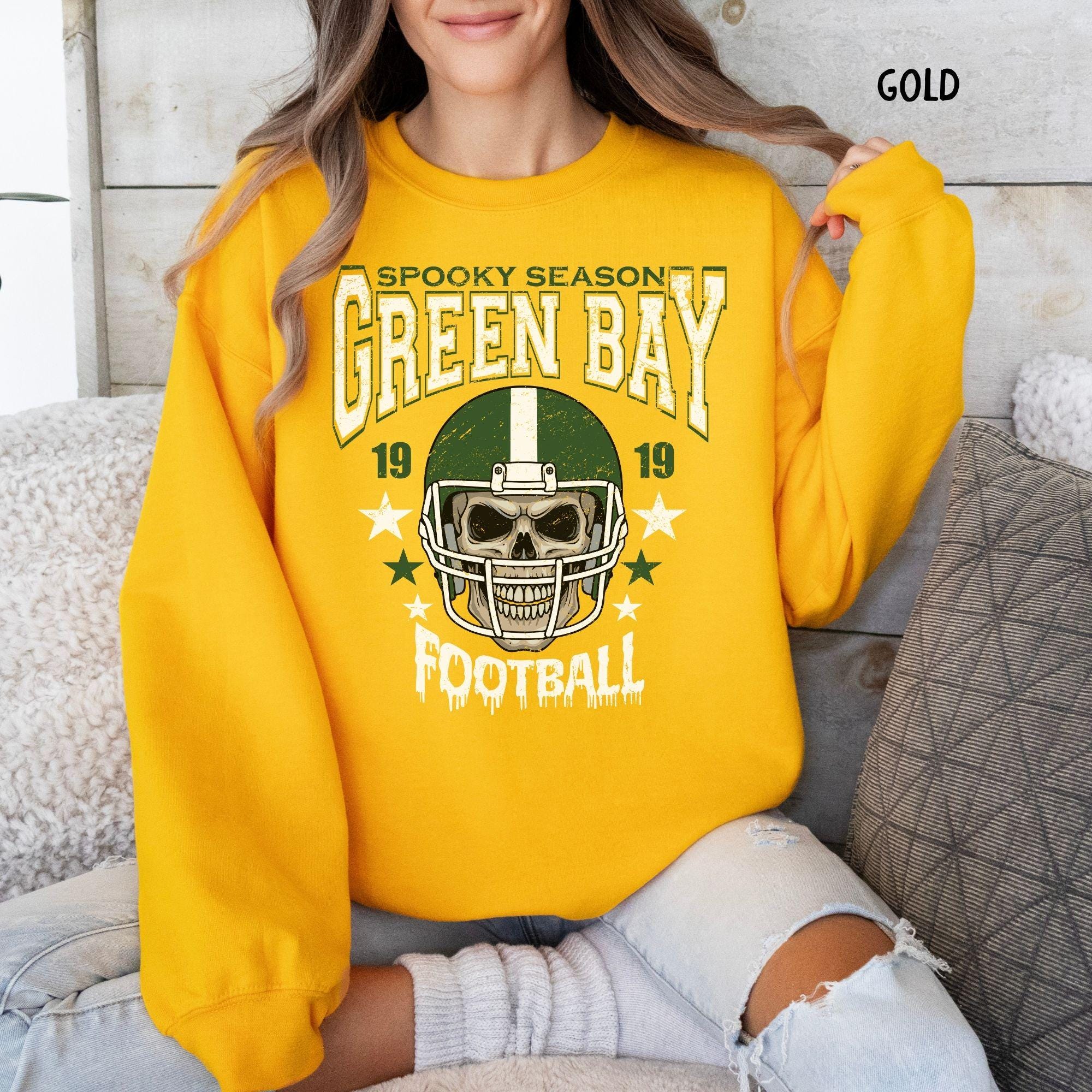 A model wearing a military green t-shirt with a Green Bay football skull design for spooky season.