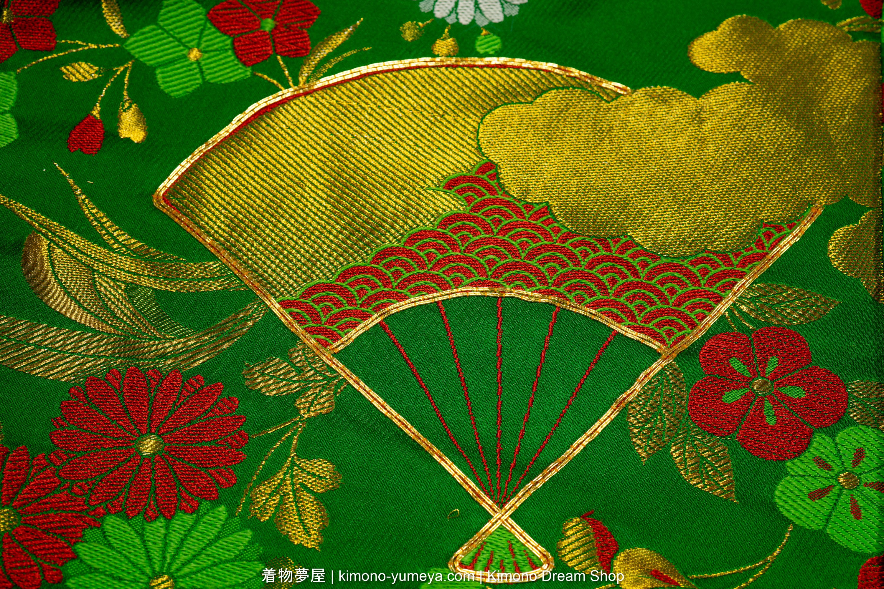 Gold folding fan with red seigaiha pattern and gold clouds inside, surrounded by flowers and clouds, all on a green background.