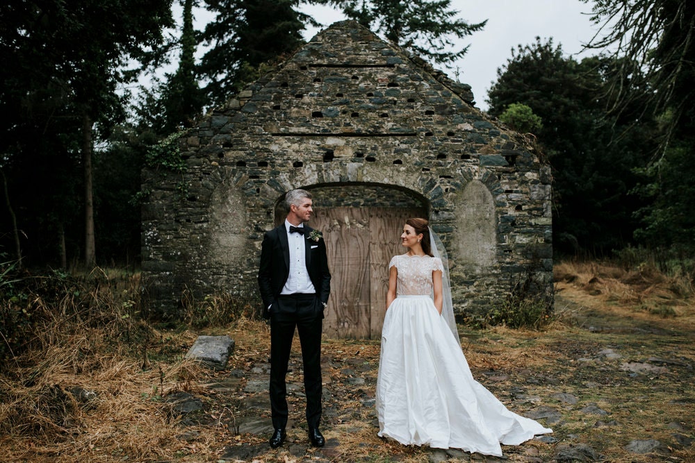 Bride and groom facing each other while standing apart against a stone building