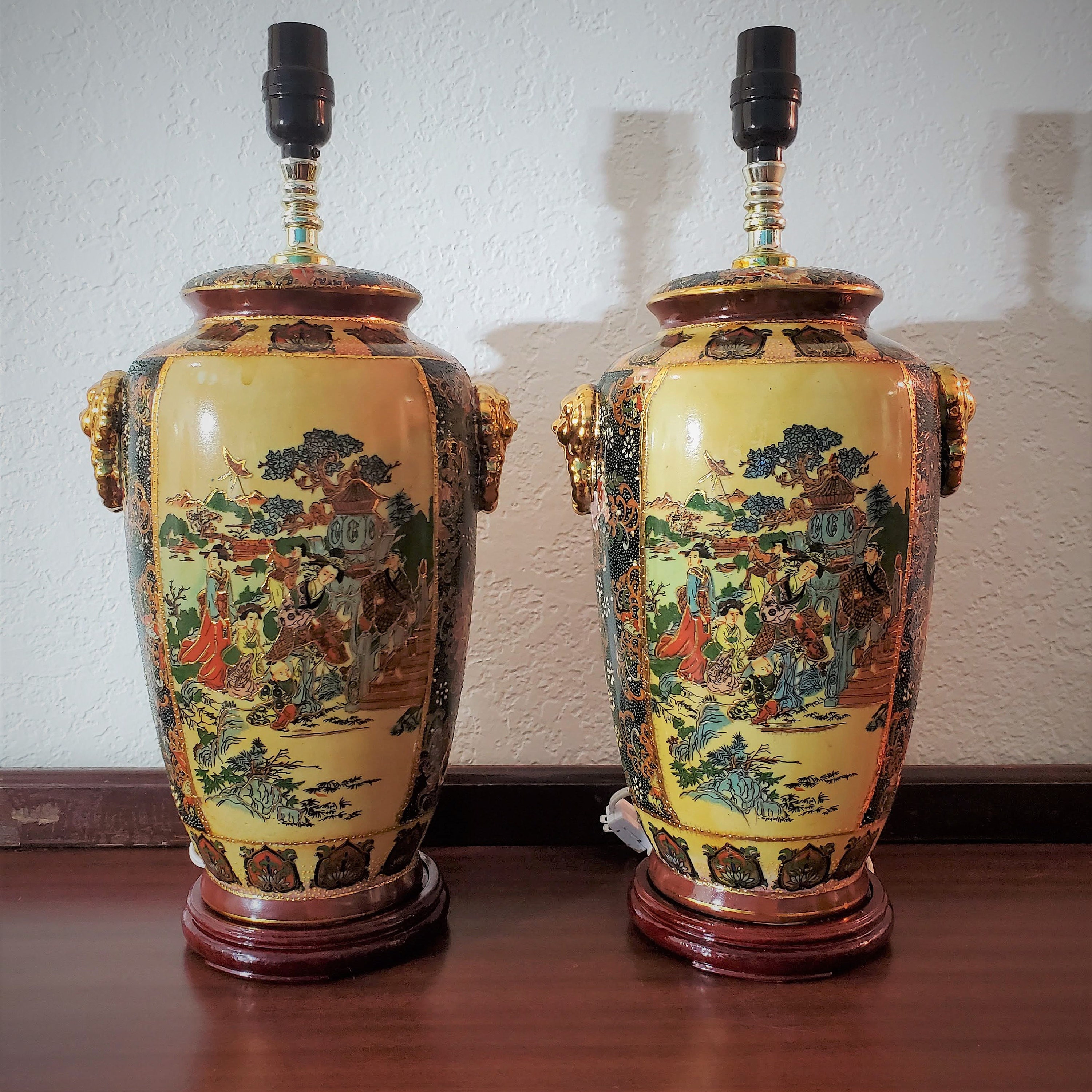 Stunning pair of Japanese Satsuma lamps, with intricate hand-painted designs in vibrant colors. These lamps exude a sense of elegance and sophistication, with their golden lion handles and matching wooden bases.