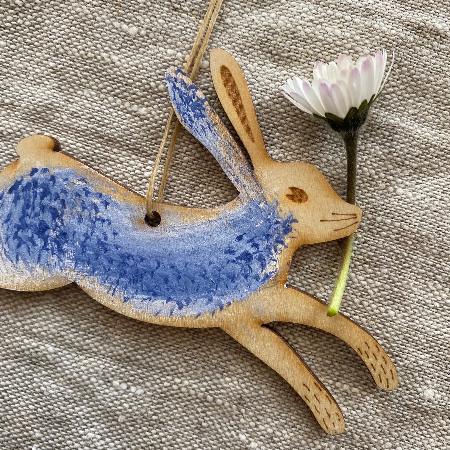 A hand painted wooden laser cut Hare easter decoration in a blue and white palette with a daisy flower