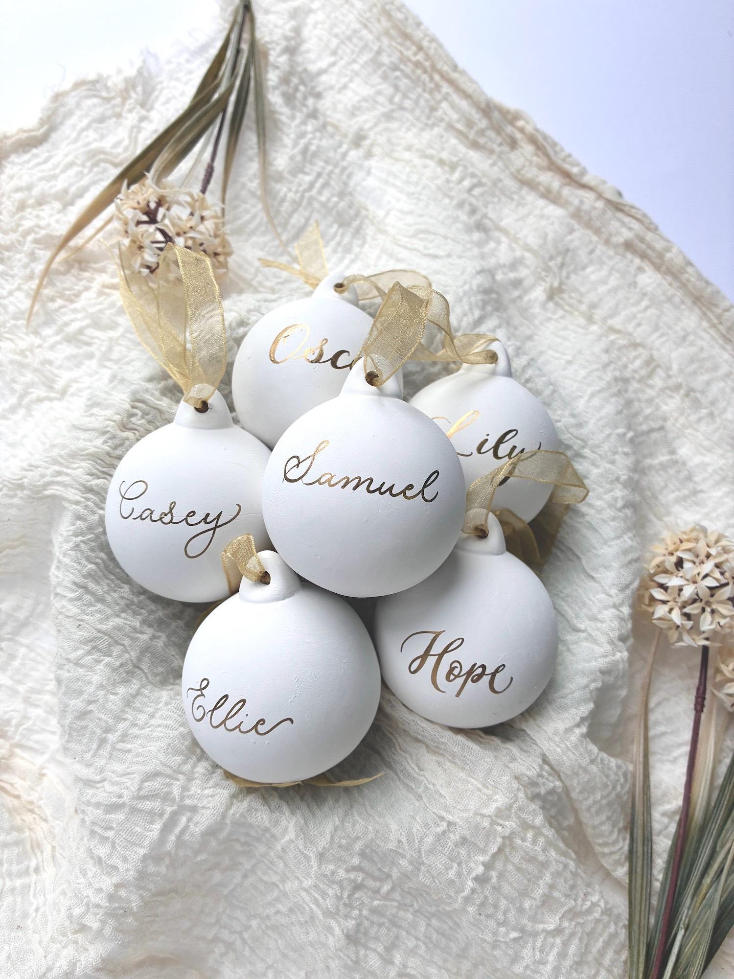 Six white Christmas baubles with names on, arranged in a bowl