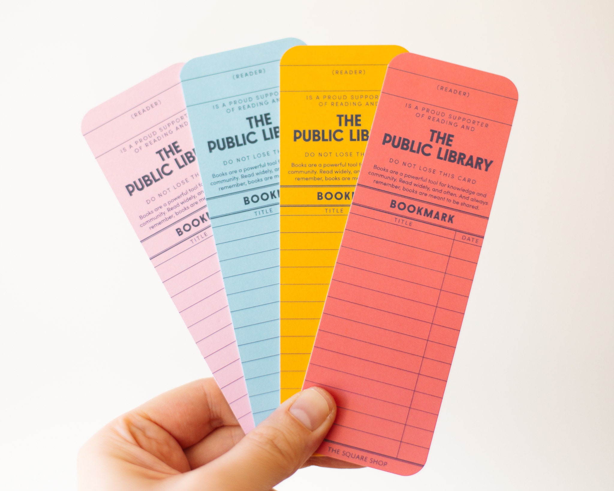 A hand holding four reading list bookmarks, one each in Pink, Blue, Yellow, and Red.