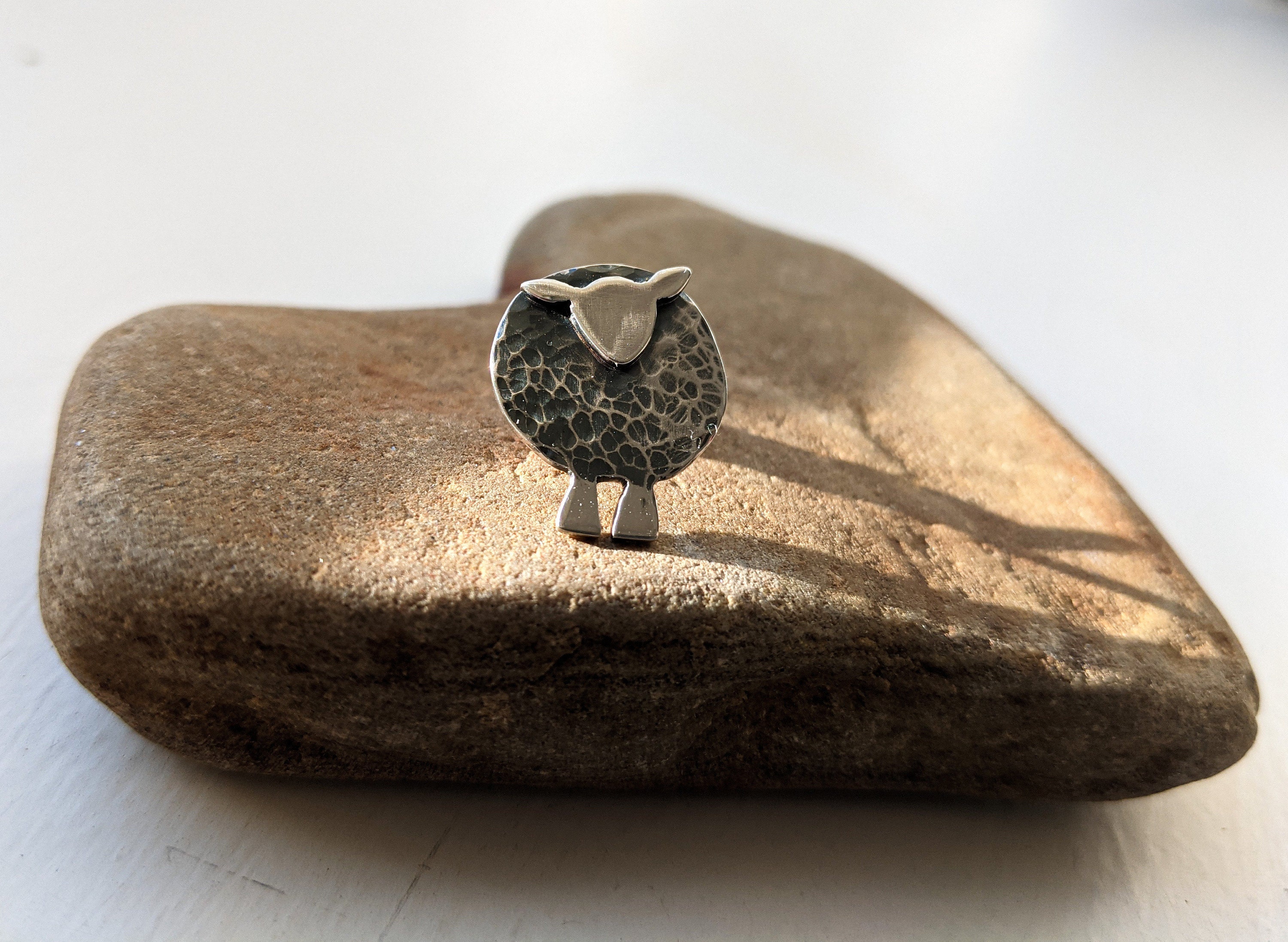 Colour photograph of a silver pin brooch in the form of a sheep.