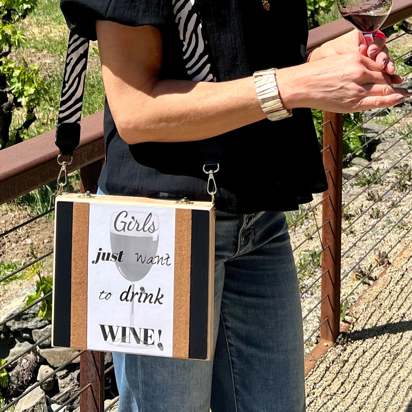 Girl in vineyard with a glass of red wine and a cigar box purse with the phrase Girls Just Want to Drink Wine! printed on it, with cork accents.