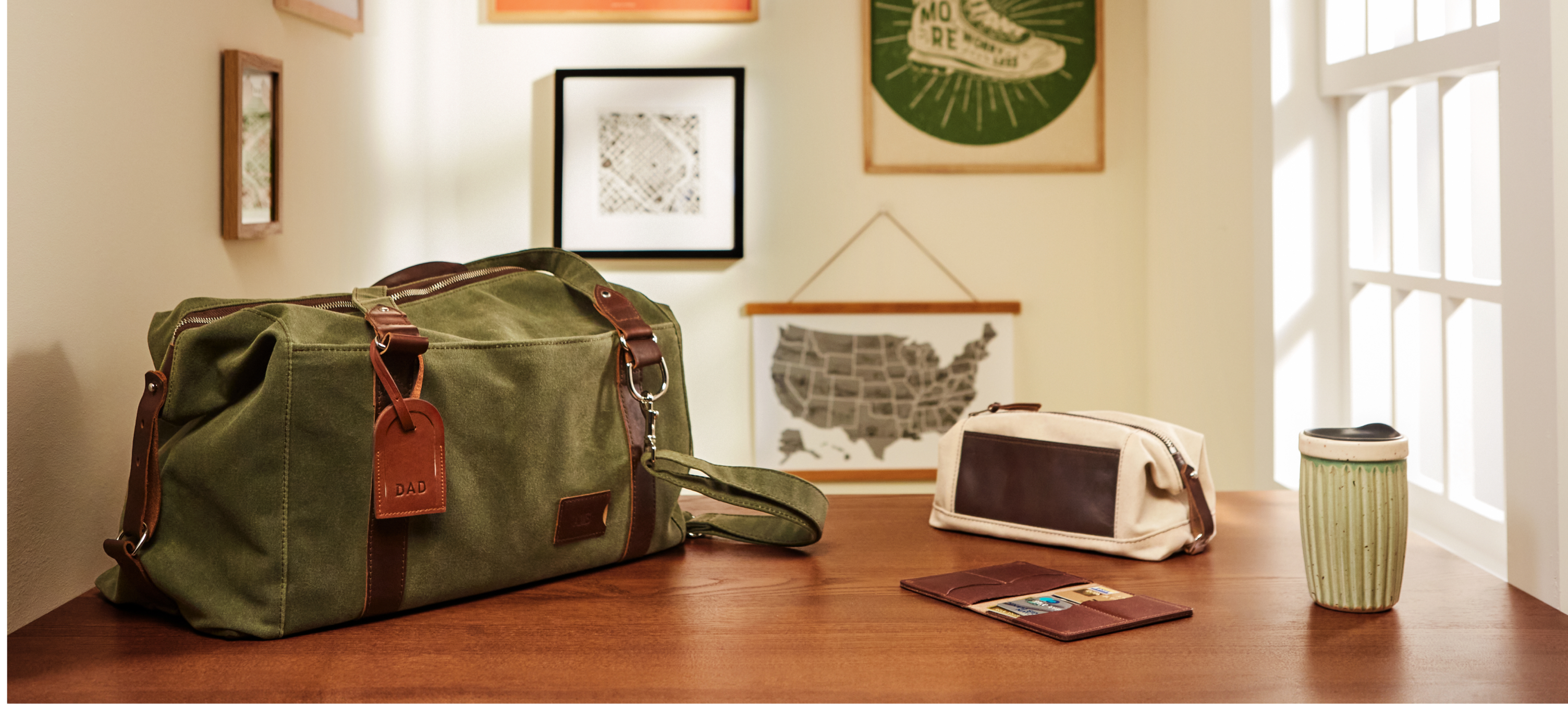 A green duffle bag, a brown leather wallet, and a white canvas bag on a wooden table